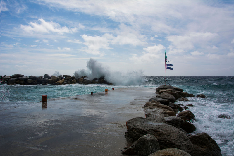 Des vagues s'écrasent contre un quai rocheux sous un ciel dramatique, montrant la puissance de la nature.