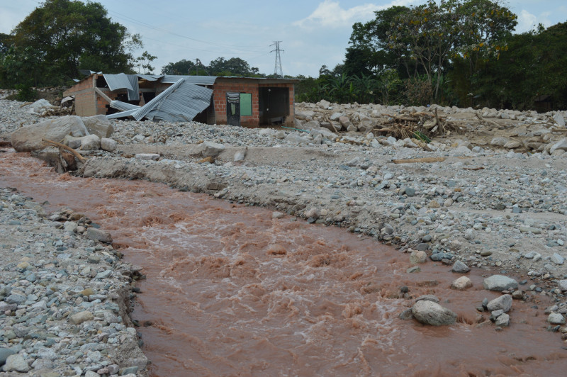 Une maison endommagée se dresse près d'une rivière boueuse après une inondation, illustrant l'impact des catastrophes naturelles.