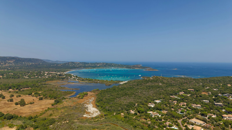 Aerial view of a turquoise bay with boats near a forested coastline