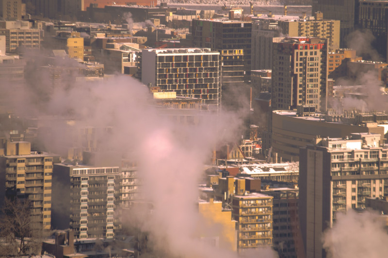 Skyline de la ville avec de la fumée s'élevant des bâtiments, illustrant une scène hivernale urbaine à Montréal.