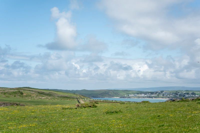 Green grassy field overlooking a coastal town under cloudy sky