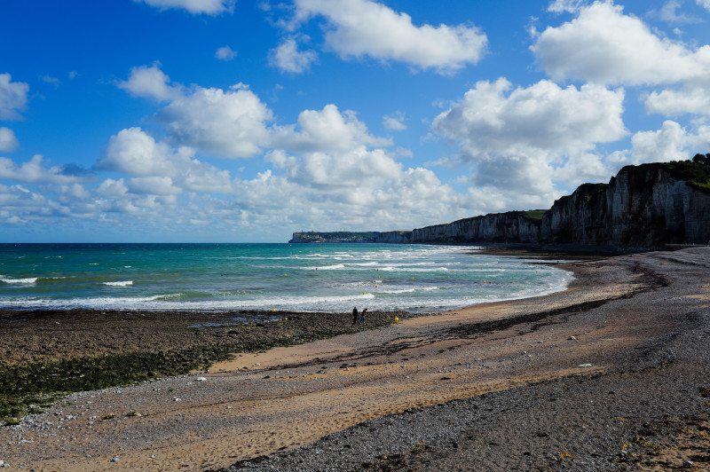 Une vue imprenable sur la côte normande avec une plage rocheuse et des falaises dramatiques sous un ciel bleu.