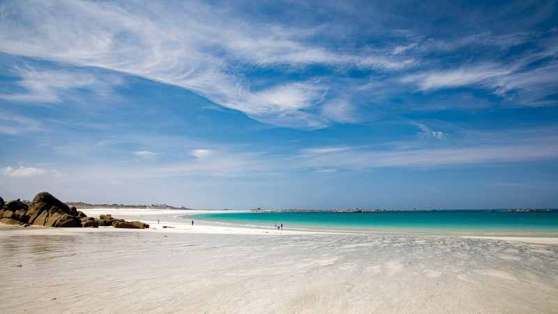 Scène de plage sereine en Bretagne, France avec un ciel clair et des eaux azurées.