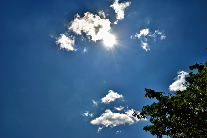 The bright sun shining in a clear blue sky with scattered white clouds