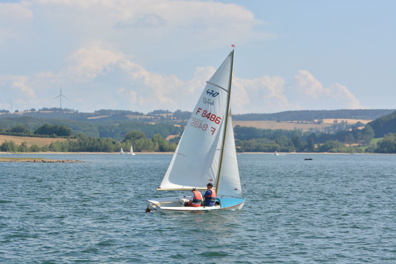 Scène sereine d'un voilier glissant sur un lac ensoleillé en Occitanie, France.