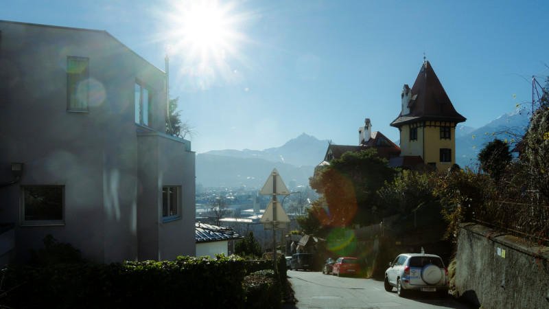 Sunlit street with a tower, modern building, and mountains