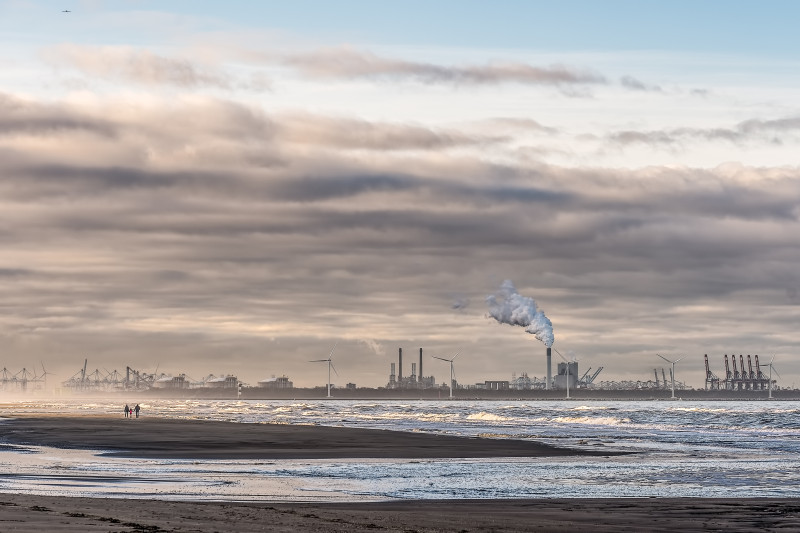 Belle photo d'une mer avec des moulins à vent et une usine au loin sous un ciel nuageux