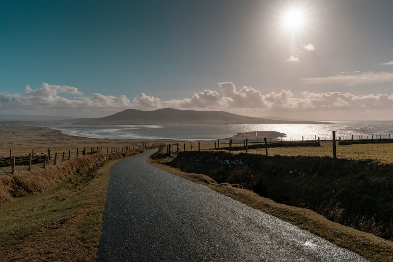 A winding road leads to a coastal landscape under sunlight