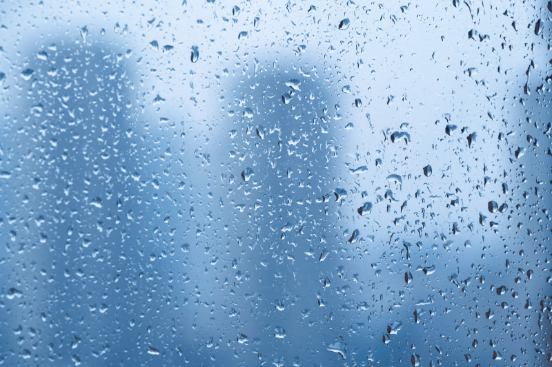 Gouttes de pluie sur une fenêtre avec un arrière-plan de paysage urbain flou créant une ambiance tranquille.