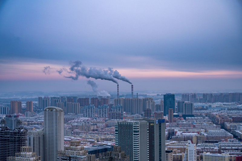 Vue aérienne de la ligne d'horizon de la ville de Harbin avec ses cheminées d'usine à l'aube, illustrant le développement urbain.