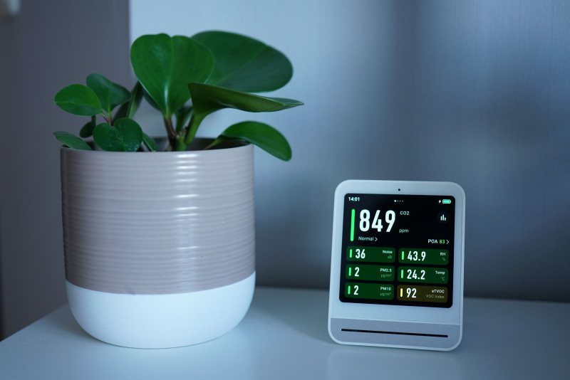 Moniteur de qualité de l'air à côté d'une plante en pot sur un bureau, indiquant les niveaux de CO2 et de PM2,5.