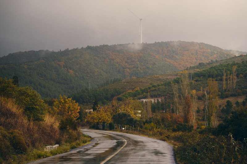 Route sinueuse à travers des collines d'automne avec un moulin à vent au loin après la pluie.