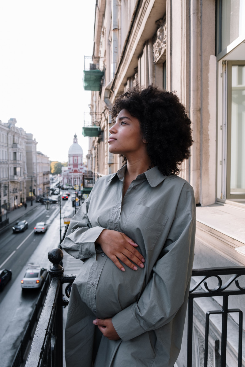 Un portrait serein d'une femme enceinte avec des cheveux afros se tenant sur un balcon surplombant une rue de la ville.