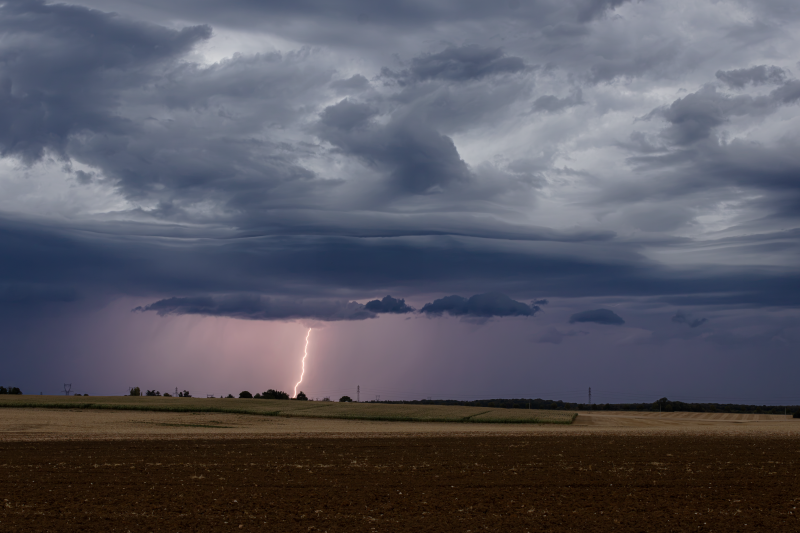 Un éclair fulgurant illumine le ciel sous les nuages ​​d'orage sombres au-dessus des champs de la campagne française.