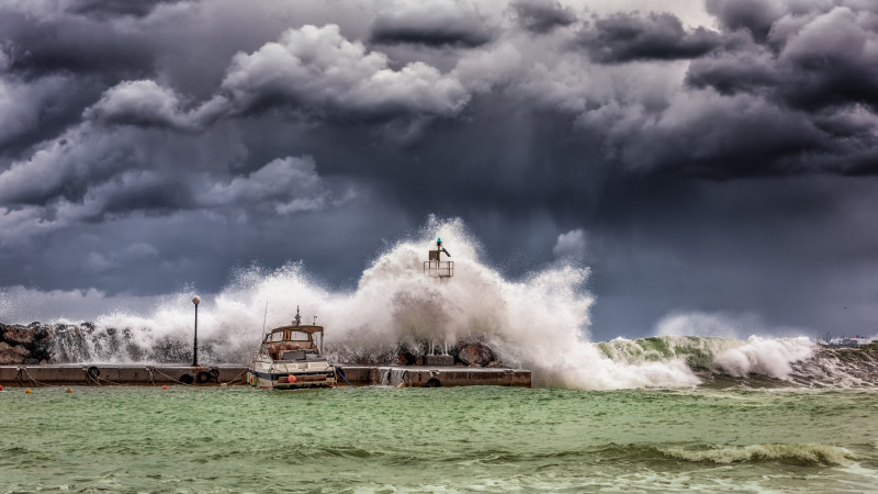 Des vagues puissantes s'écrasent contre un quai et un phare sous des ciels orageux sombres.