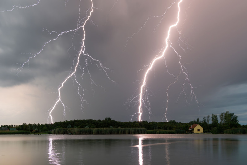 Superbe capture de plusieurs éclairs frappant un lac calme pendant une tempête à la tombée de la nuit.