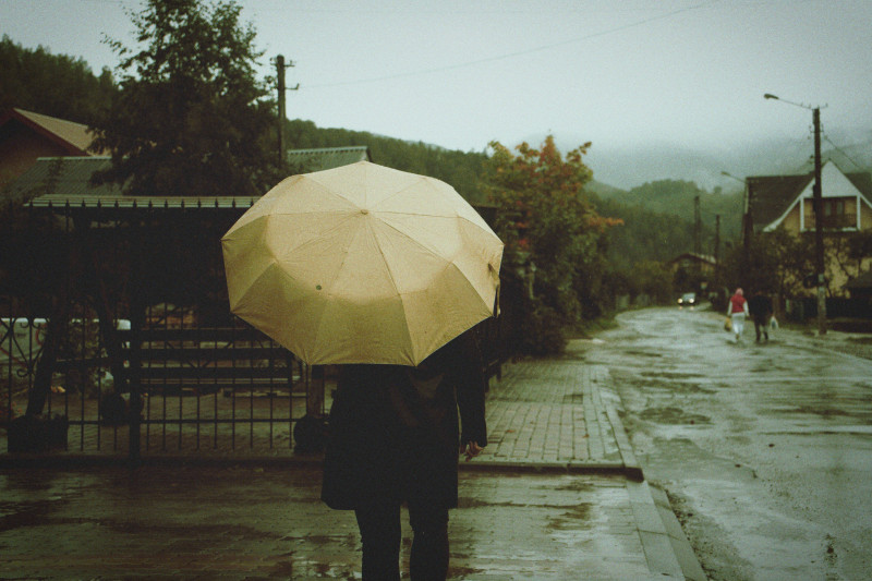 Une personne marche sous un parapluie dans une rue de la ville sous la pluie, évoquant une atmosphère mélancolique.