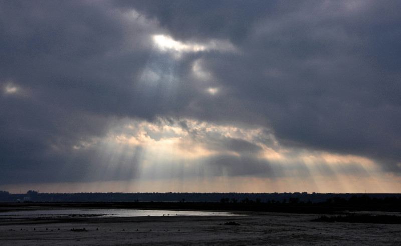 The sun shines through the clouds over a body of water