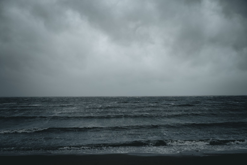 Une scène dramatique des vagues océaniques sous un ciel nuageux et mélancolique, créant une atmosphère sereine mais intense.