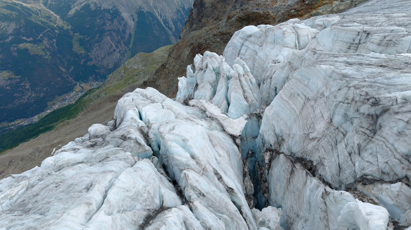 A deep crevasse in a white glacier above a green mountain valley