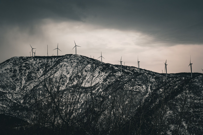 Des montagnes enneigées avec des éoliennes sous des cieux dramatiques, mettant en avant l'énergie renouvelable dans la nature.