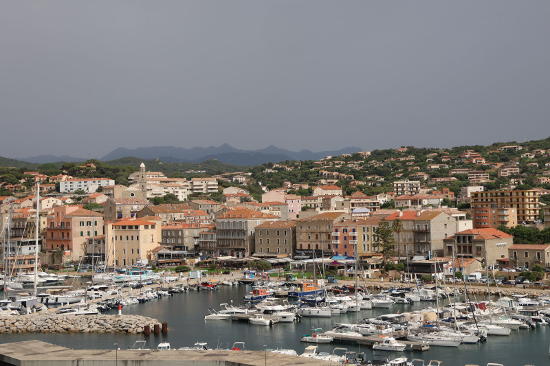 Magnifique vue du port de Propriano avec des bateaux et des bâtiments historiques, sur fond de paysage vallonné en Corse.